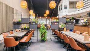 Ein modernes Restaurant mit hohen Tischen, orangefarbenen Stühlen und hängenden Korbstühlen.