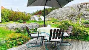 A wooden deck with a table and chairs, an umbrella, and a rock garden. - 4 Star Holiday Home in Ellos (Ellos)