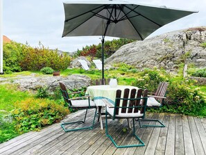A wooden deck with a table and chairs, an umbrella, and a rock garden. - 4 Star Holiday Home in Ellos (Ellos)