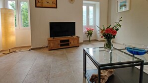 Ein Wohnzimmer mit Flachbildfernseher auf einem Holzboden, einem Glastisch und einer Vase mit Blumen.