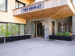 The exterior of The Heimat hotel with a modern design, featuring a wooden slatted roof, stone facade, and black planters with greenery. - Apartment in Schrocken Near Ski Arlberg (Schroecken)