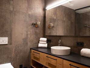 A modern bathroom with a round sink, wooden vanity, and a large mirror. - Apartment in Schrocken Near Ski Arlberg (Schroecken)