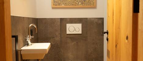Un baño moderno con lavamanos, inodoro y un dispensador de papel higiénico de pared.