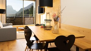 A modern dining area with a wooden table, black chairs, a black pendant light, and a vase with flowers. A large window offers a view of mountains. - Apartment in Schrocken Near Ski Arlberg (Schroecken)