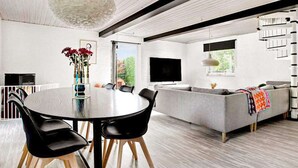 A modern living room with a round dining table, black chairs, a grey sofa, and a staircase.