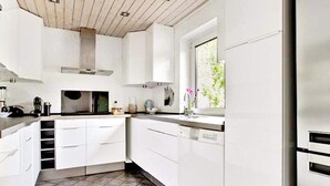 A modern kitchen with white cabinets, a tiled floor, and a window with a view of greenery.