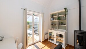 Una habitación luminosa con una puerta corrediza de vidrio que da a un espacio al aire libre, un armario blanco con puertas de cristal, un estufa de leña negra y un sofá negro.
