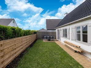 A residential property with a fenced backyard, a patio area with outdoor furniture, and a white building with large windows.
