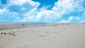 Una extensa playa de arena con cielo despejado y algunas nubes dispersas.