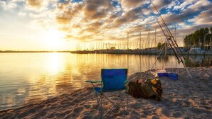 Une plage avec une chaise et des cannes à pêche, un lac paisible et un coucher de soleil.