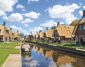 A canal-side row of traditional houses with thatched roofs, a wooden dock, and a clear sky.