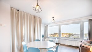 A modern room with a round table, blue chairs, a sofa, and large windows offering a view of the beach. - Studio in Oostduinkerke With Sea View (Koksijde)