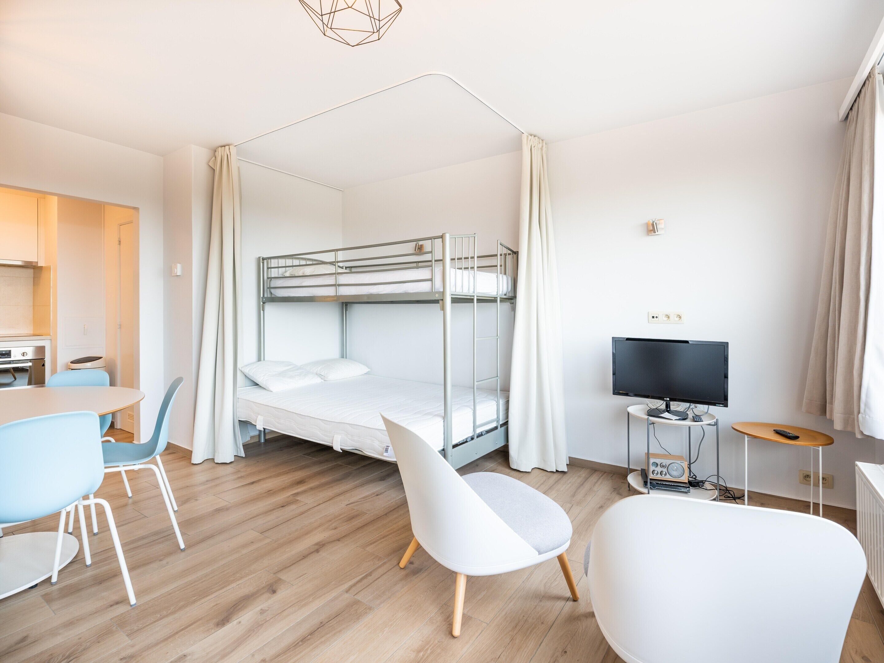 A modern hotel room with a bunk bed, a dining area with a table and chairs, a television, and a small radio.