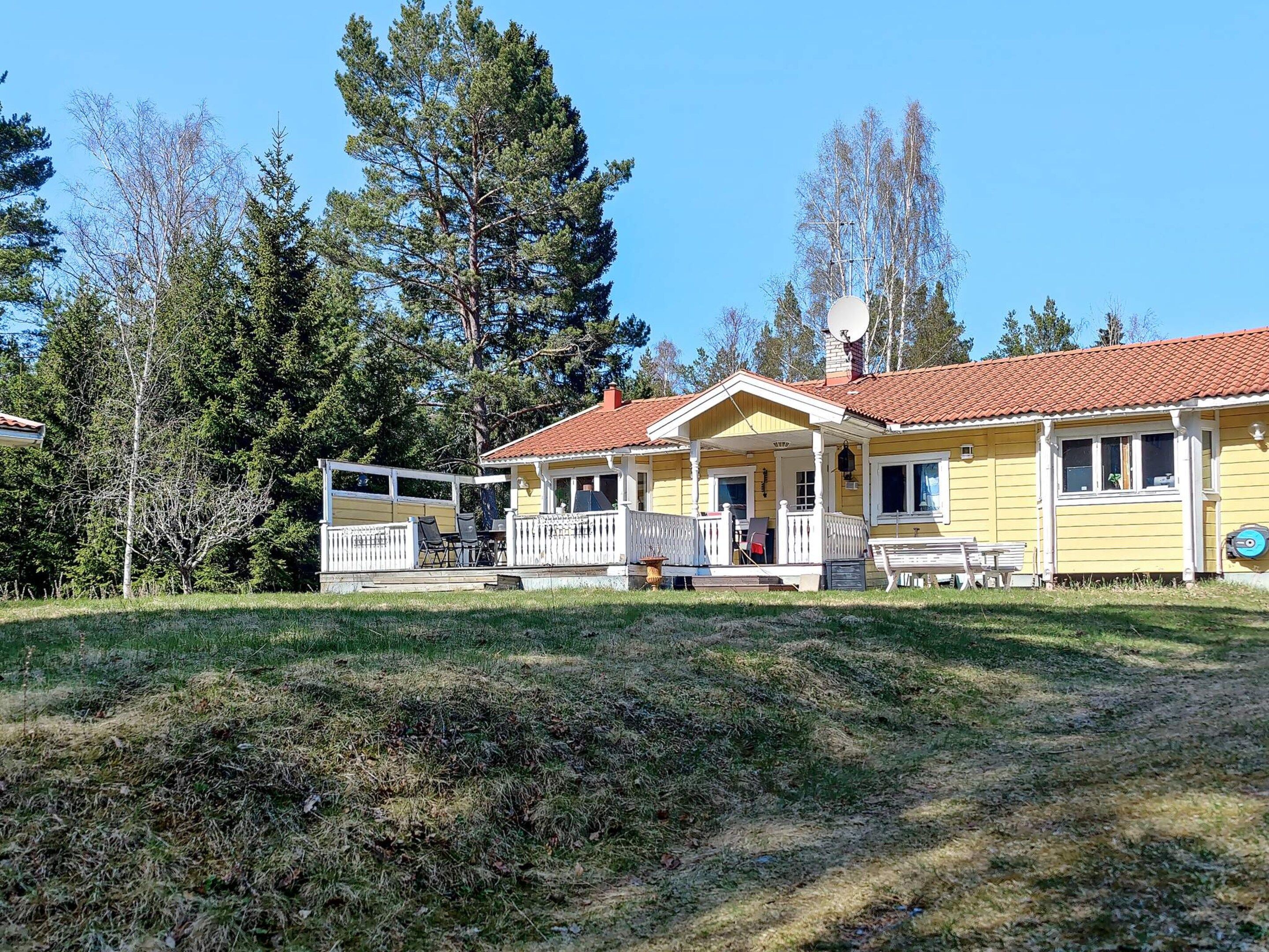 A two-story yellow house with a red-tiled roof, a porch with white railings, and a satellite dish.