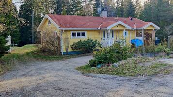 A yellow house with a red roof, a porch, and a gravel driveway.
