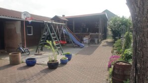 A courtyard with a play area, including a slide and a swing set, surrounded by potted plants and a bicycle.