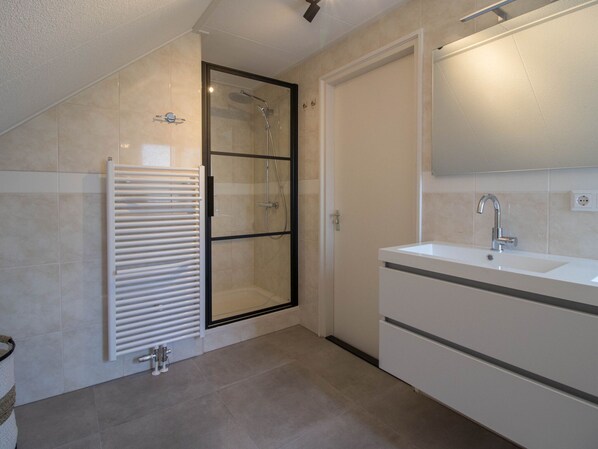 A modern bathroom with a glass-enclosed shower, a white radiator, and a large mirror above a sink. - Modern Villa in Makkum With Garden (Makkum)