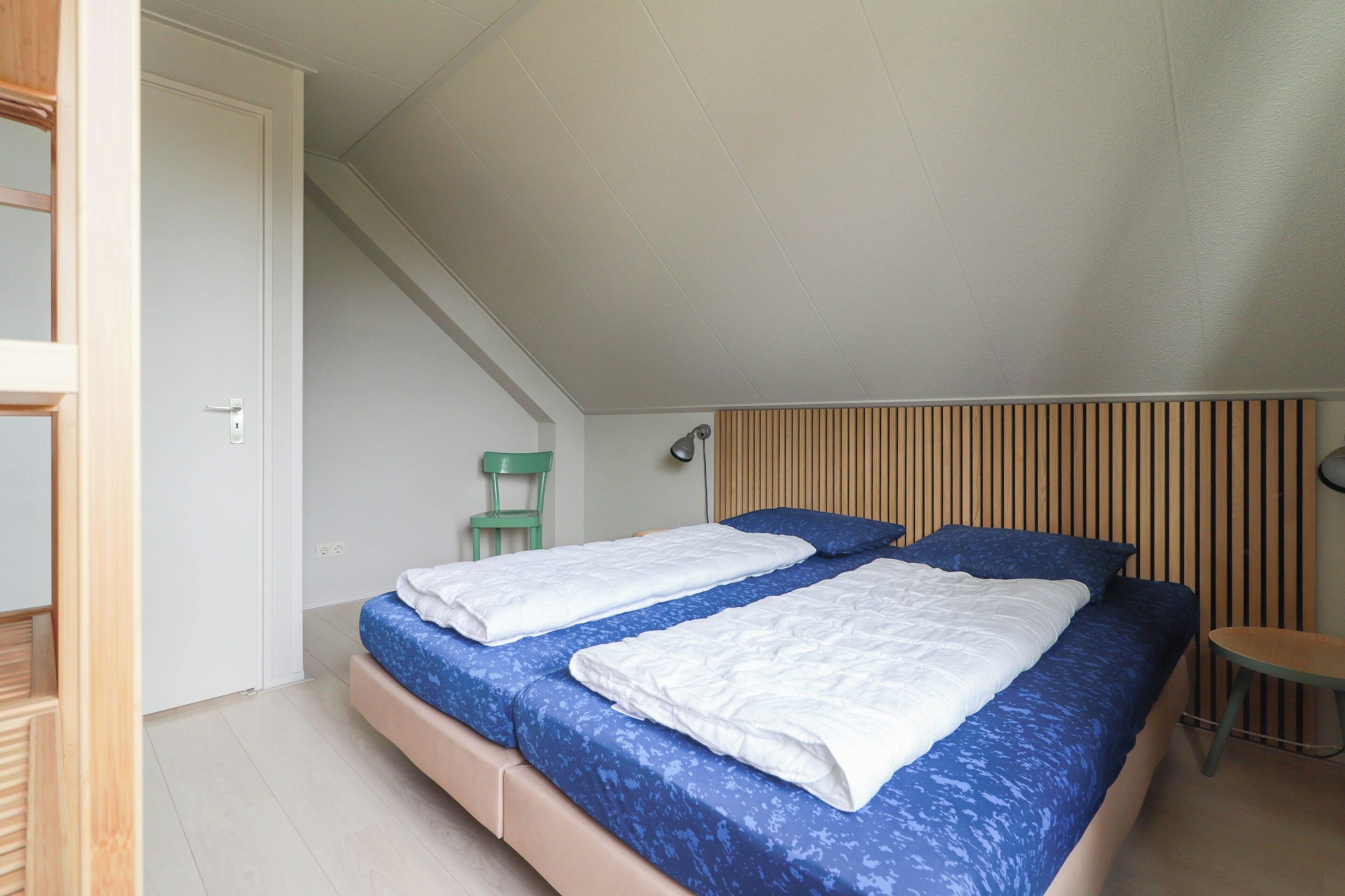 A bedroom with two beds, a chair, a desk, and a sloped ceiling.