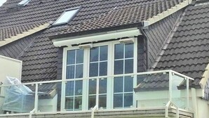 A residential building with a sloped roof, a large window with a white frame, and a balcony with a white railing. - Maisonnette met Charme (Scharbeutz)