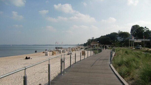 A wooden boardwalk leading to a sandy beach with a railing on one side and a grassy area on the other. - Maisonnette met Charme (Scharbeutz)