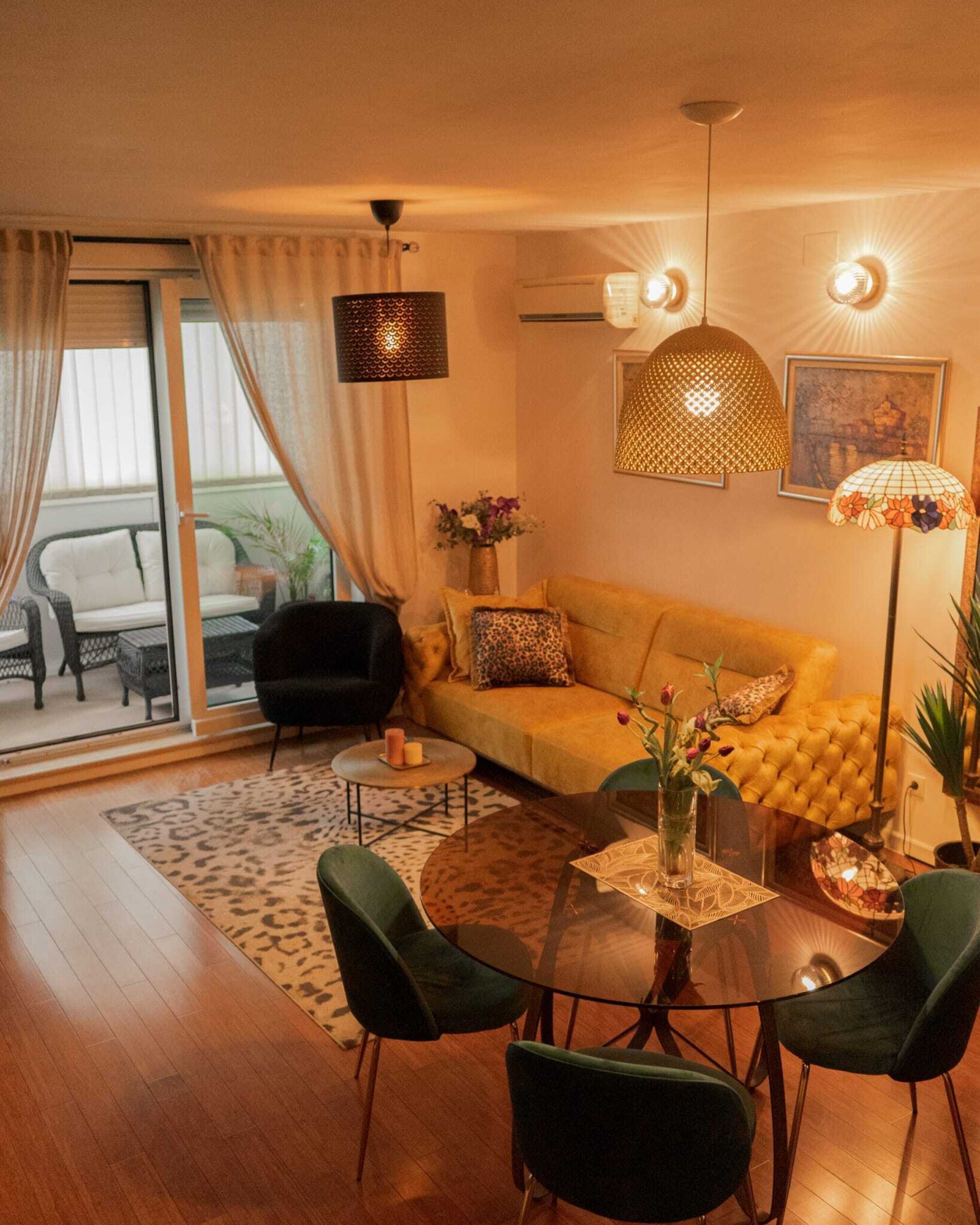 Een moderne woonkamer met een bank, groene stoelen, een glazen salontafel en een eettafel.