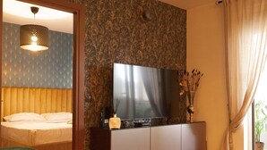 Een hotelkamer met een bed, een televisie op een kastje, een spiegel en een raam met gordijnen.