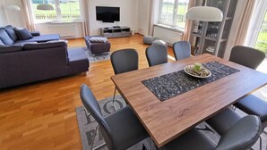Una sala moderna con sofá, mesa de comedor, sillas, televisor y vistas al exterior.