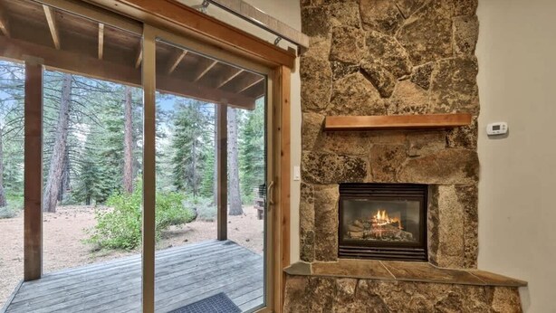 A stone fireplace with a fire, a wooden shelf above it, and a glass door leading to an outdoor deck.