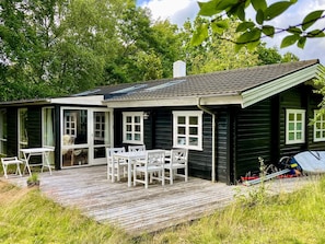 A small wooden house with a deck, white furniture, and a bicycle.