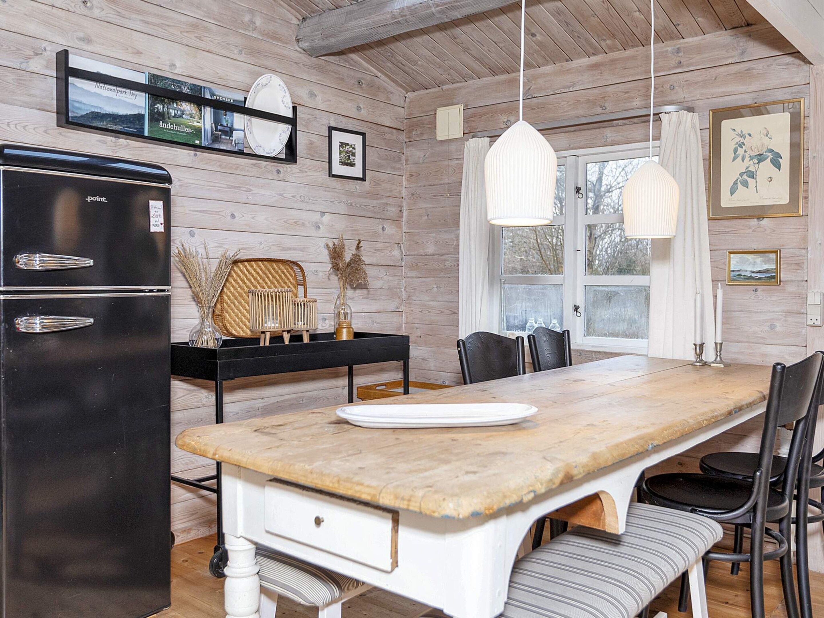 Een houten interieur met een keukenhoek, inclusief een zwarte koelkast, een eettafel met stoelen en een hanglamp.