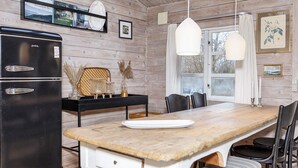 Un interior de madera con cocina, que incluye un refrigerador negro, una mesa de comedor con sillas y una lámpara colgante.