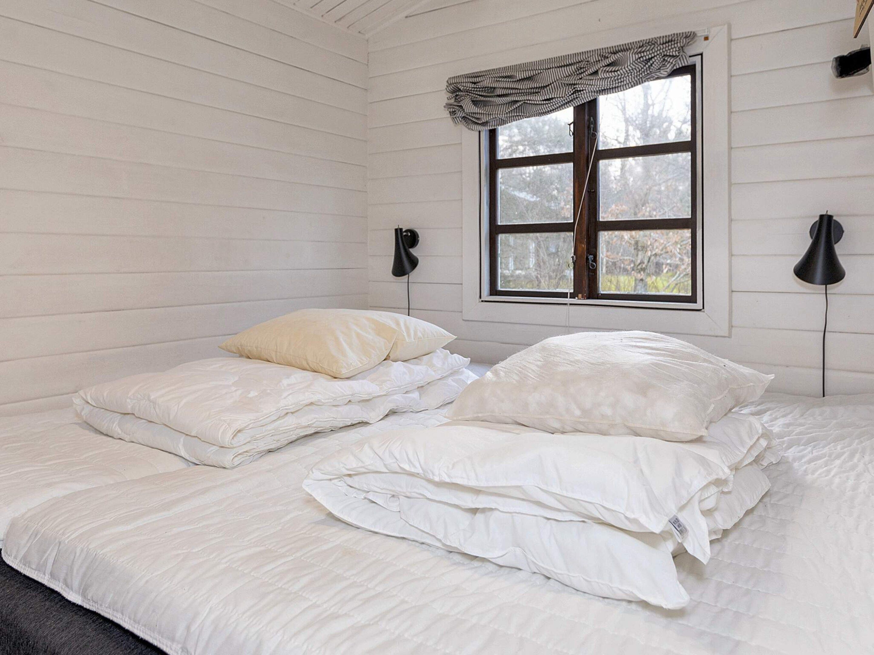 A room with a bed, two bedside lamps, a window with a curtain, and a view of trees outside.
