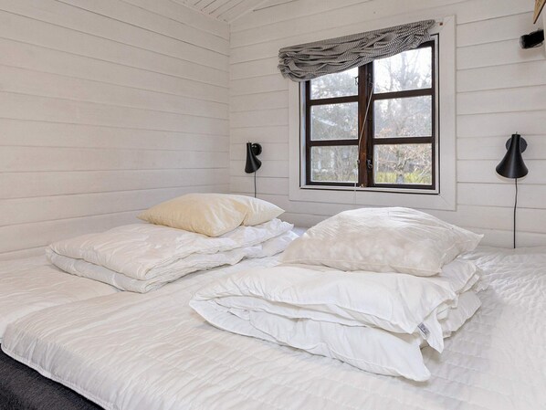 Ett rum med en säng, två sänglampor, ett fönster med gardin och utsikt över träd utanför.