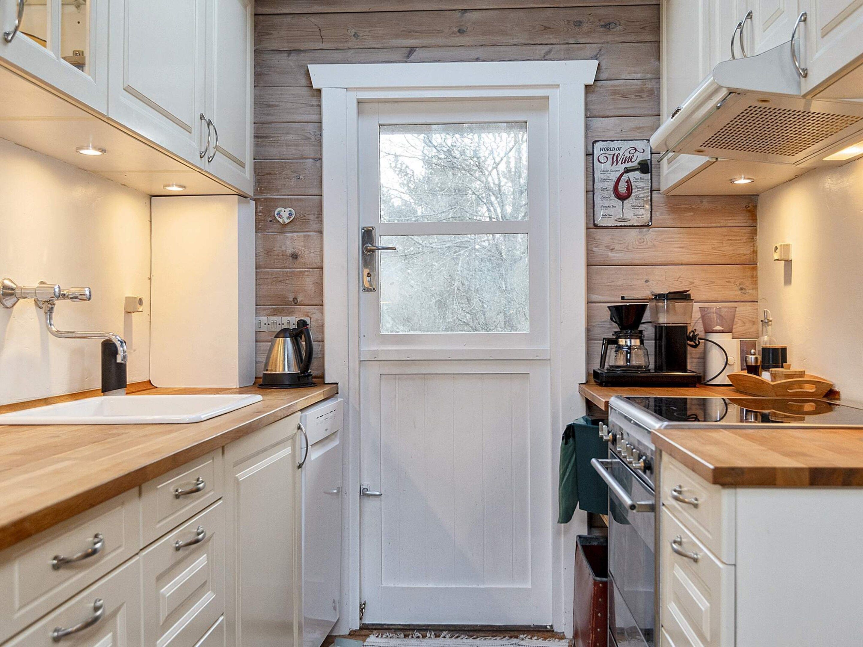 Una cocina compacta con armarios blancos, encimera de madera, cafetera y hervidor.