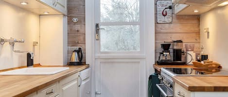 A compact kitchen with white cabinetry, a wooden countertop, a coffee machine, and a kettle.