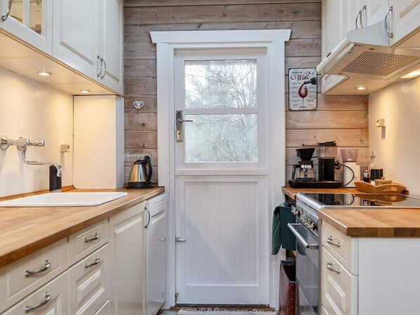 A compact kitchen with white cabinetry, a wooden countertop, a coffee machine, and a kettle.