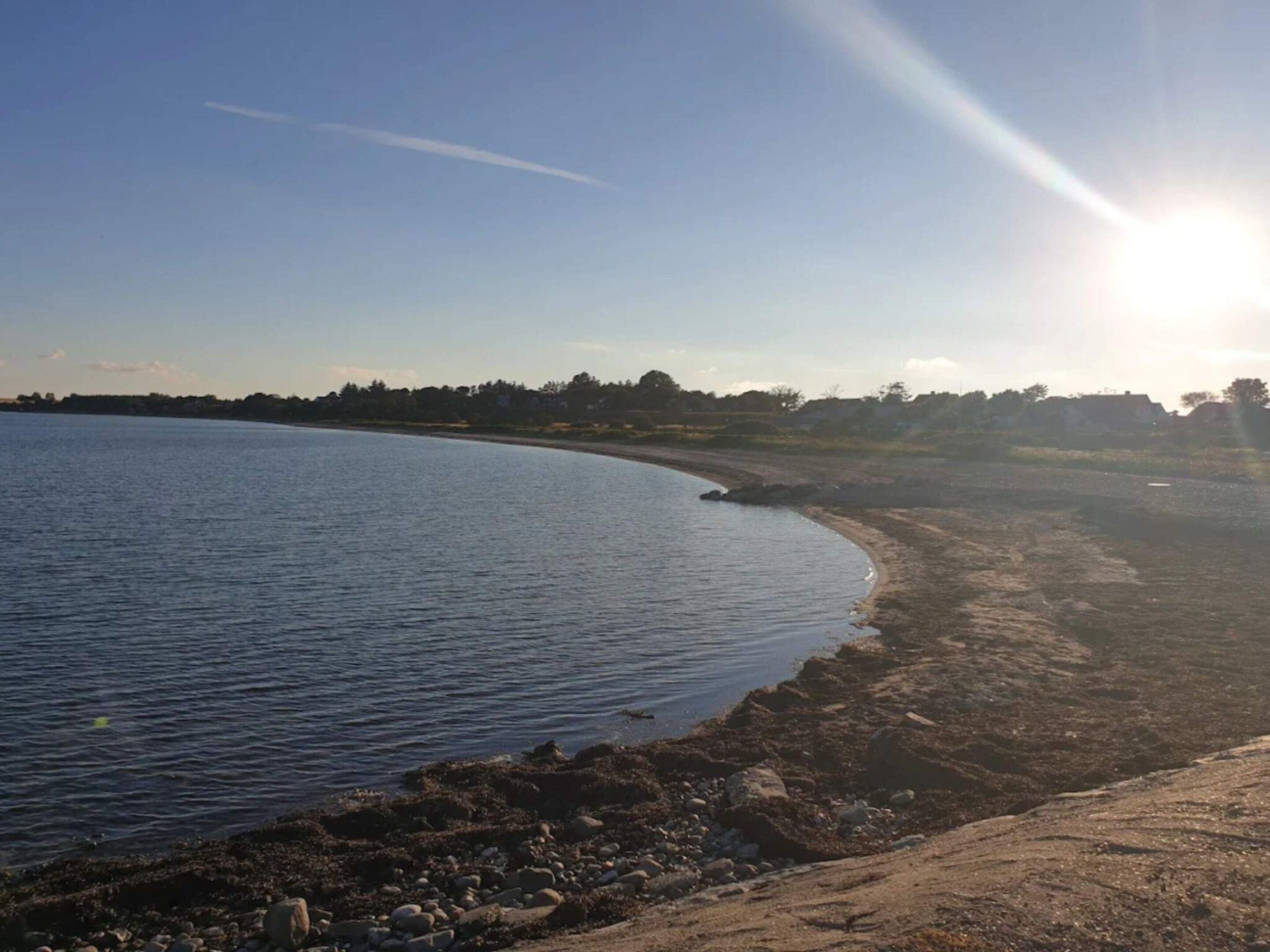 A coastal landscape with a sandy beach, calm water, and a clear sky.
