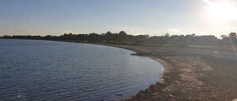A coastal landscape with a sandy beach, calm water, and a clear sky.