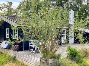 A wooden deck with outdoor seating, a black building with white windows, and a white chimney. - 5 Person Holiday Home in Veslos (Vesløs)