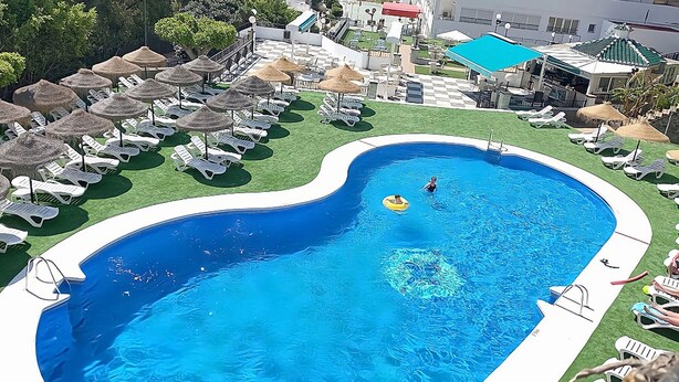 Una piscina con borde en forma de corazón, rodeada de sillas y sombrillas de descanso.