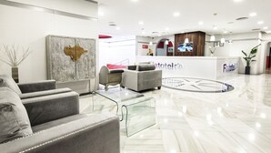 Un moderno vestíbulo de hotel con recepción, zona de estar y un elemento decorativo en la pared.