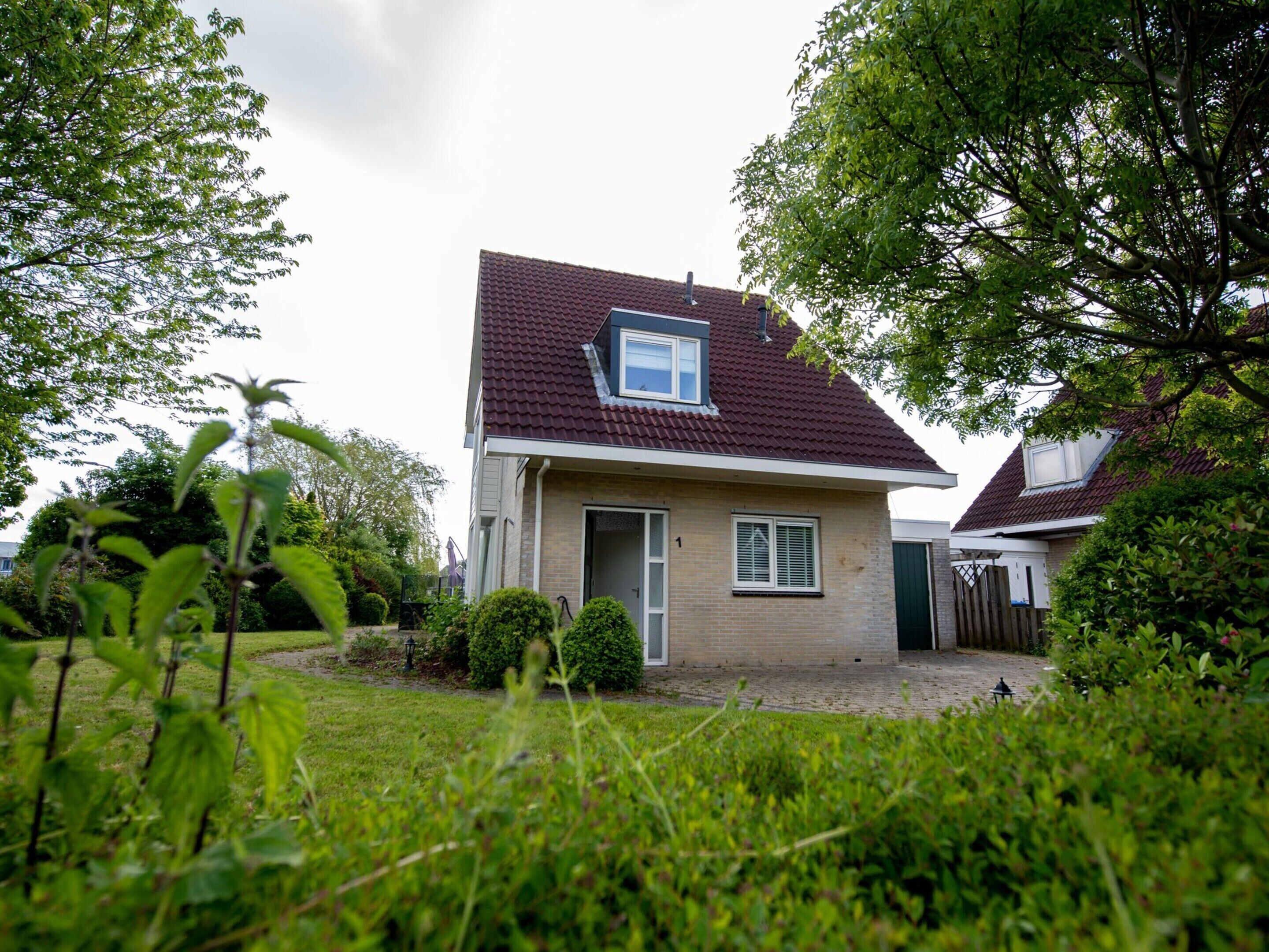 A two-story house with a red-tiled roof, a small attached garage, and a front yard with a lawn and bushes.