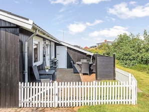 Une rangée de cabanes en bois, avec une clôture blanche devant, un patio aménagé avec du mobilier d’extérieur et un ciel dégagé.