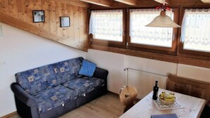 Una habitación acogedora con un sofá estampado, una mesa con una botella y un cuenco de fruta, y un techo de madera con vigas a la vista.