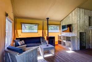 A cozy room with a sofa, a small table, a TV, and wooden shelves. - Chic Glamping Escape With Pool (Dalfsen)