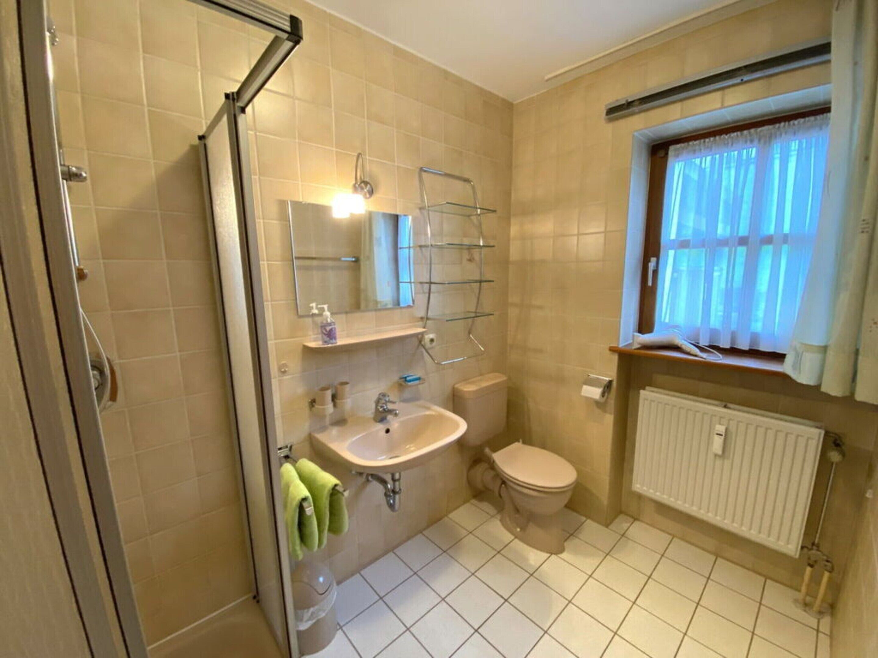 A bathroom with a shower, sink, toilet, and a window with curtains.