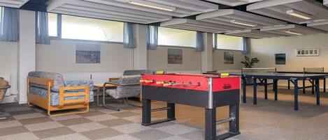 A room with a foosball table, a sofa, and a ping pong table.