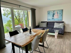 A modern living room with a wooden dining table, grey sofa, and a painting on the wall. - Apartment in Kaprun Near Ski Slopes (Piesendorf)