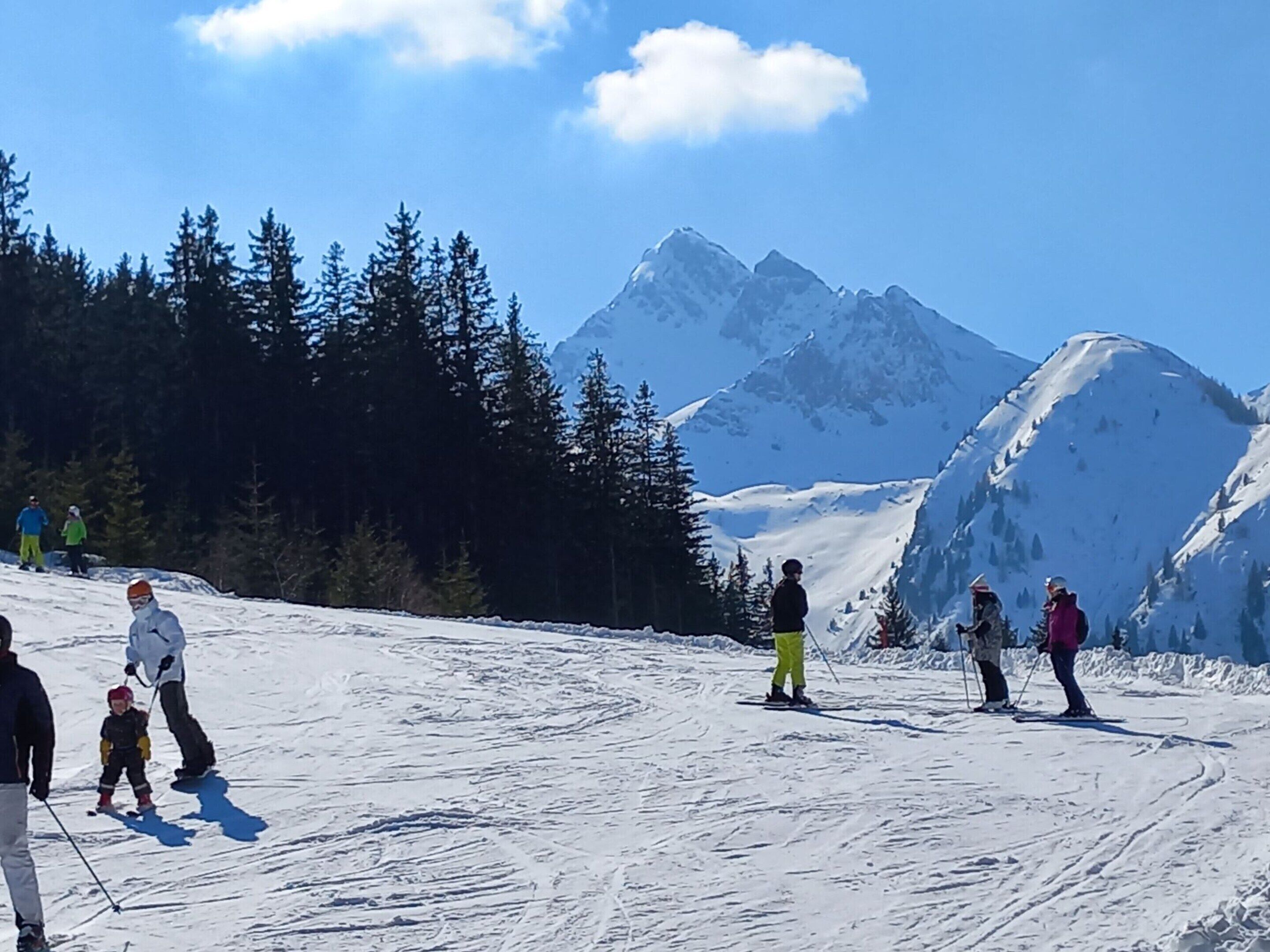 A snowy ski slope with skiers and a mountain backdrop.
