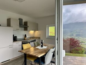 A modern kitchen with a dining table, chairs, and a view of the countryside through a large window. - Apartment in Kaprun Near Ski Slopes (Piesendorf)